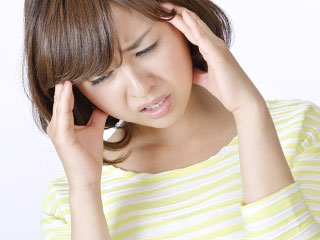 不快そうに頭を押さえる女性