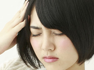 辛そうに頭を押さえる女性