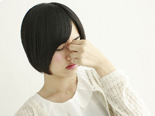 眉間を指で押さえる女性
