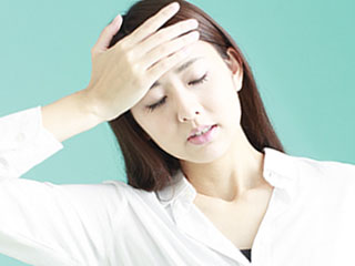 だるそうに頭を押さえる女性