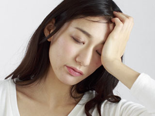 額を片手で押さえて目を閉じる女性