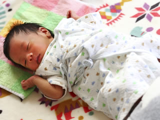 温かい毛布に包まれ眠る新生児