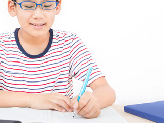 ノートに書く眼鏡を掛けた小学生