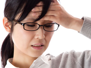 額を手で押さえながら疲れた表情の女性