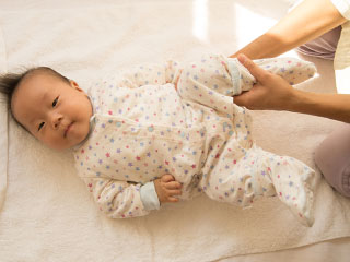 赤ちゃんの脚を掴んで動かす女性