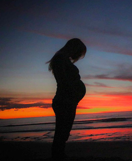 夕日を背景に立つ妊婦