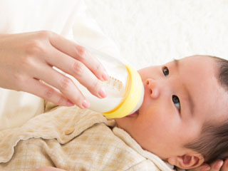 哺乳瓶を持って赤ちゃんに飲ませる母親
