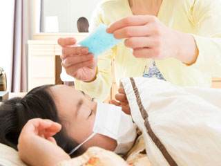 寝る子供の額に熱さましシートを貼る母親