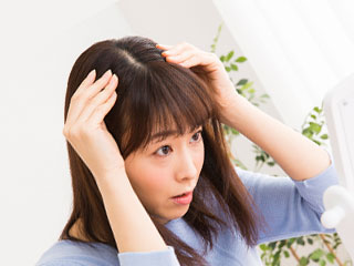 髪の分け目を鏡で見つめる女性