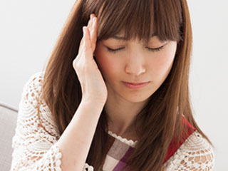 頭痛で頭に手を当てる女性