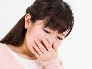 吐き気で口を手で塞ぐ女性