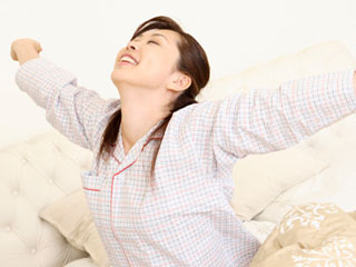 朝、寝台に座って体を伸ばす女性