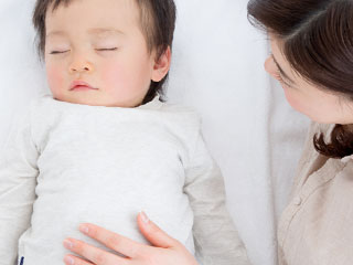 眠る赤ちゃんのお腹に手を置く母親
