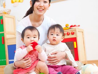 保育園で保育士に抱かれる幼児