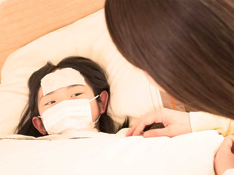 母親に看病されマスクをして布団に寝ている女の子