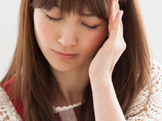 こめかみを押さえて目を閉じる女性