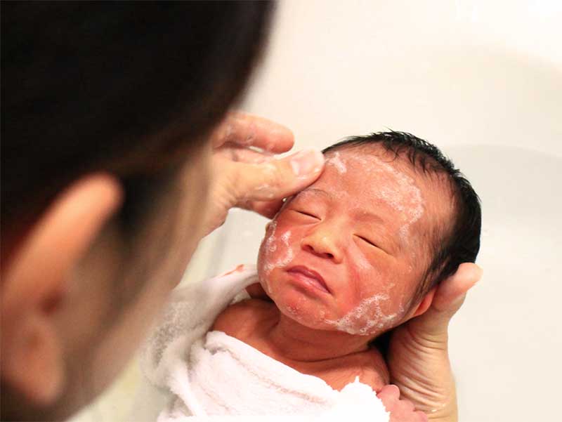 沐浴で顔を洗われている新生児