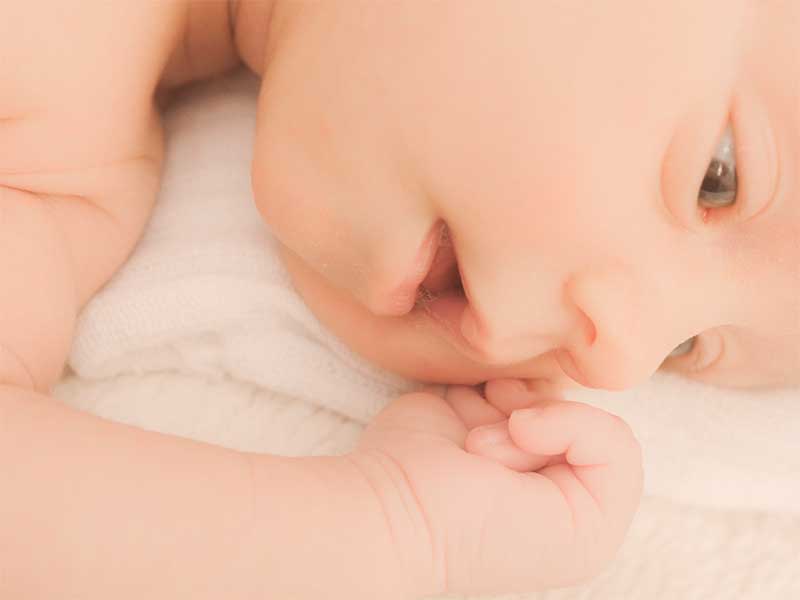 ほっぺたを手でかいている新生児