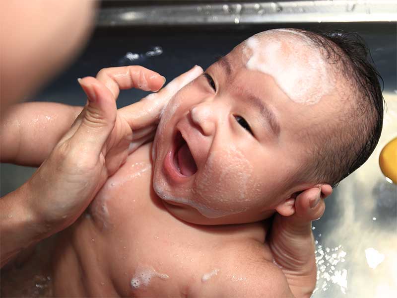 沐浴で顔を洗ってもらって笑顔の新生児