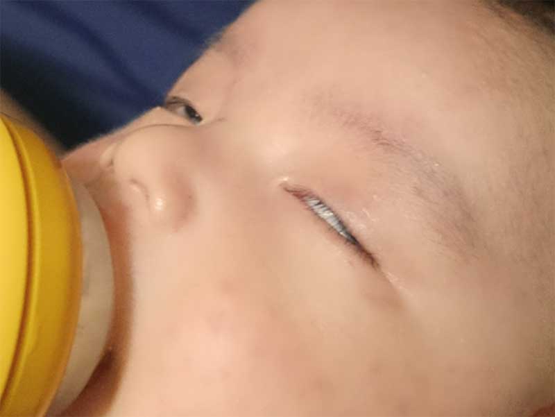 白目で寝ながら哺乳瓶でミルクを飲んでいる新生児