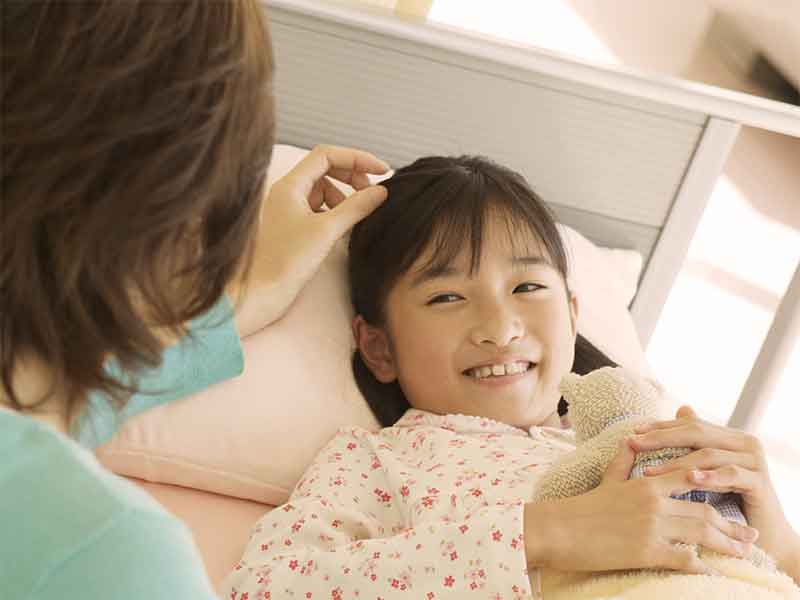 布団で横になっている女の子の頭をなでてあげる母親