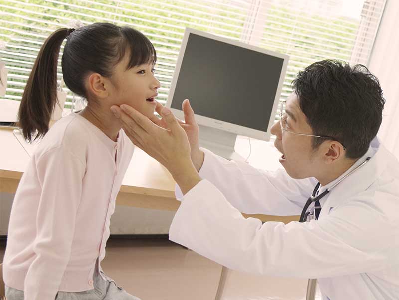 女の子の首にできたしこりの硬さを確認している男性医師