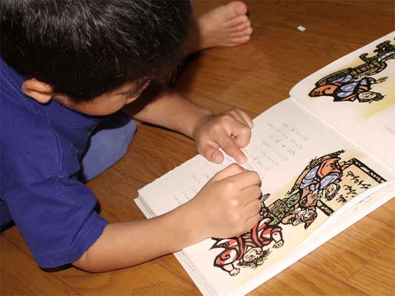 床で無理な体勢で絵本を読んでいる子供