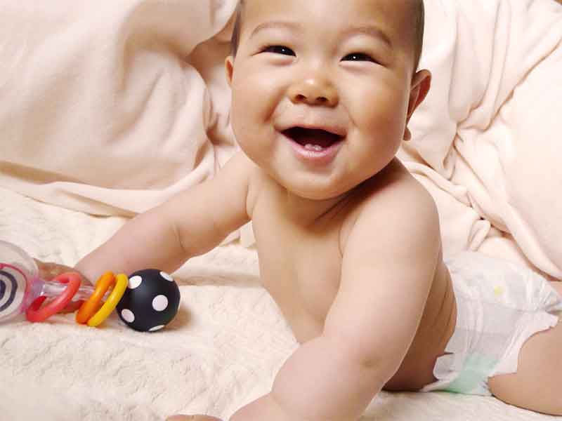 片手におもちゃを持って上半身を起こしている6ヶ月の赤ちゃん