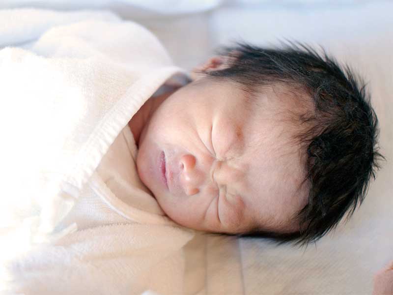 床に苦しそうな顔で寝ている新生児
