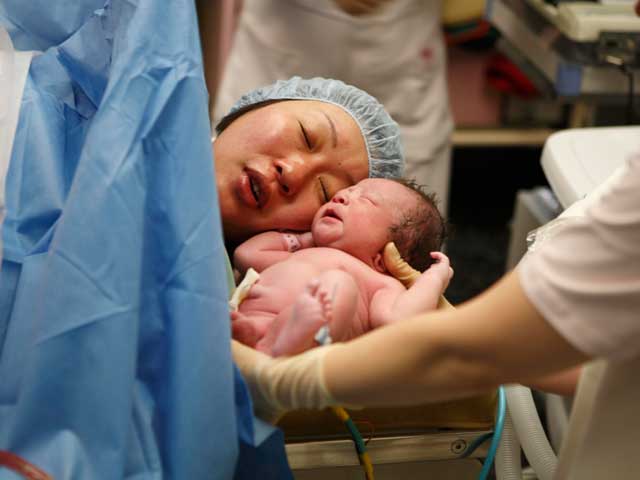 分娩台で生まれたばかりの赤ちゃんを見る女性