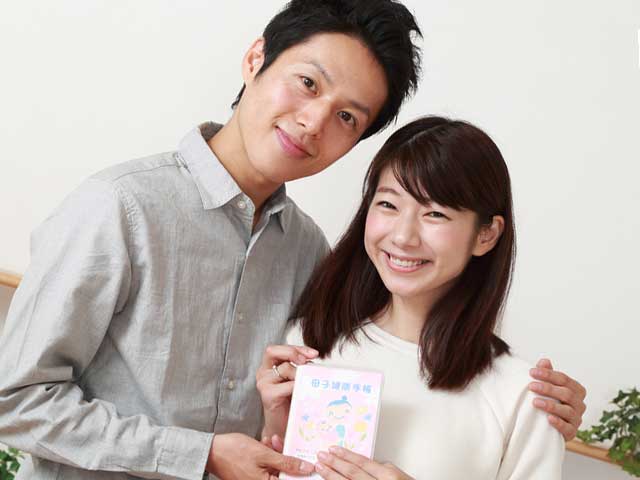 夫婦で並んで母子健康手帳を持つ