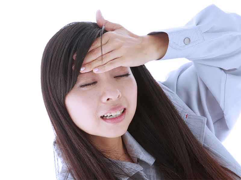 熱っぽくて額を押さえている女性