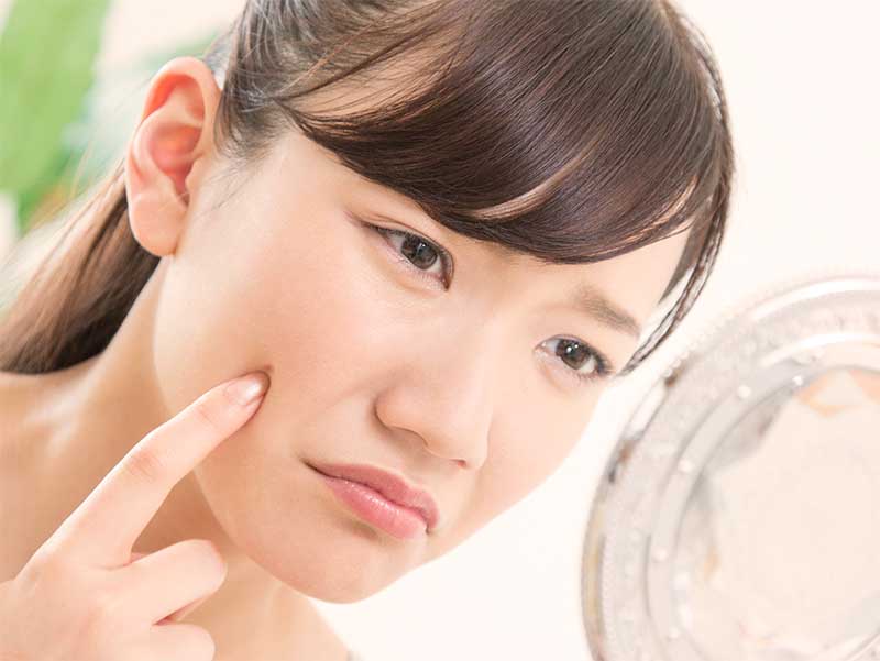 鏡で頬にできたニキビを確認している若い女性