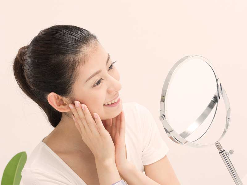 鏡で自分の顔を見て笑顔の女性