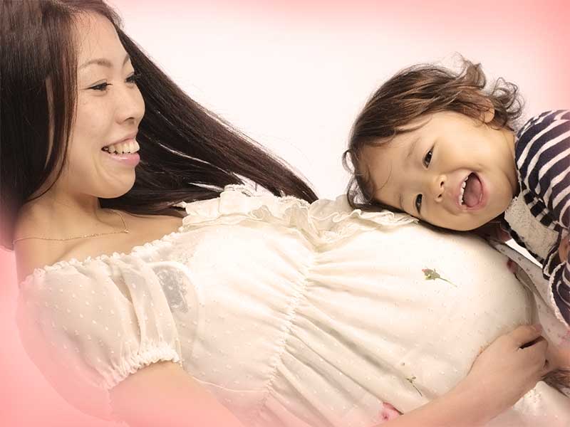 二人目を妊娠している母親のおなかに耳をあてている上の子供