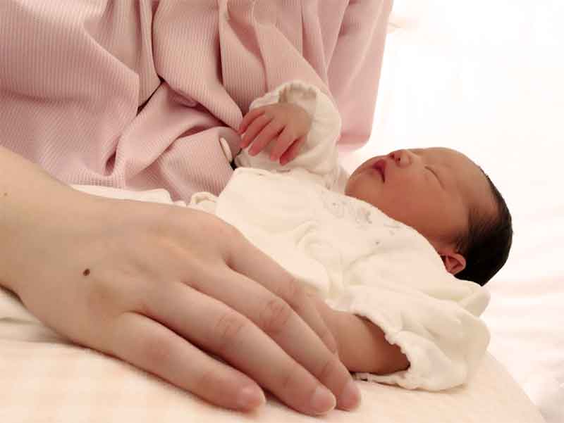 寝てる新生児に手を添えるママ