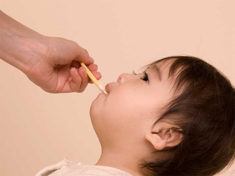 母親からスプーンで薬を飲まされてる赤ちゃん