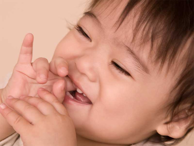 指しゃぶりをして笑顔の赤ちゃん
