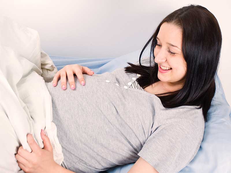 病院のベッドでお腹を押さえてる出産間近の妊婦さん