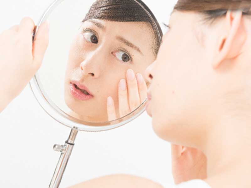 鏡を見ながら顔のニキビを気にしている女性