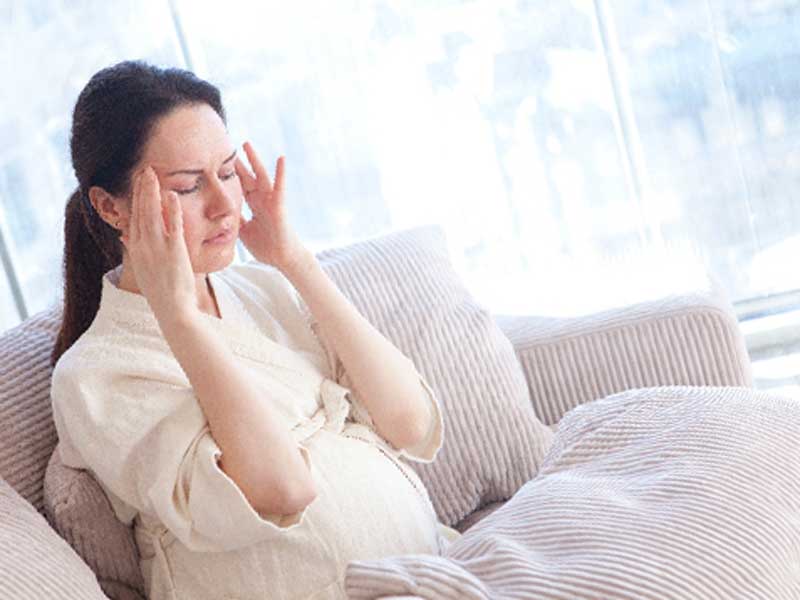 頭痛でこめかみをおさえている妊婦さん