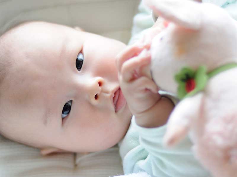寝転びながらおもちゃで遊んでいる赤ちゃん