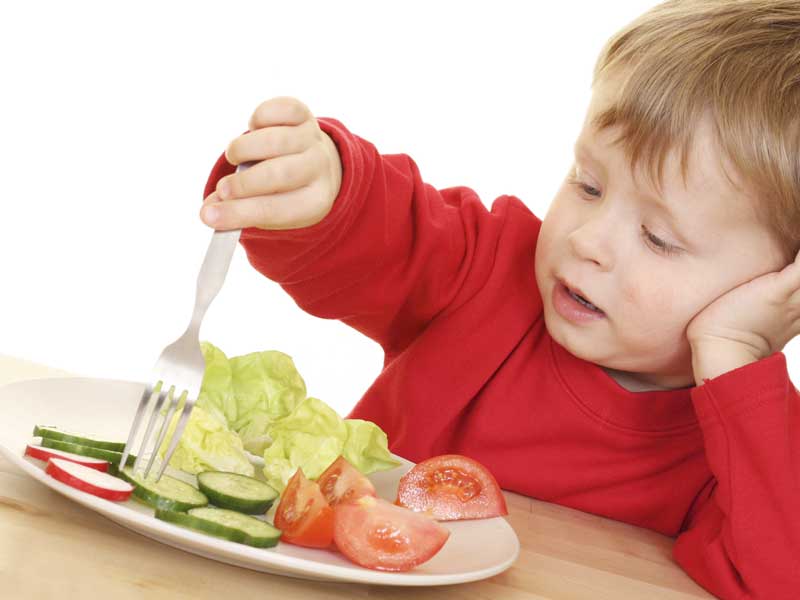 嫌そうな顔をしてフォークで野菜を刺してる子供