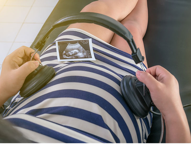 お腹にヘッドフォンをあてて胎児に音楽を聞かせる妊婦さん