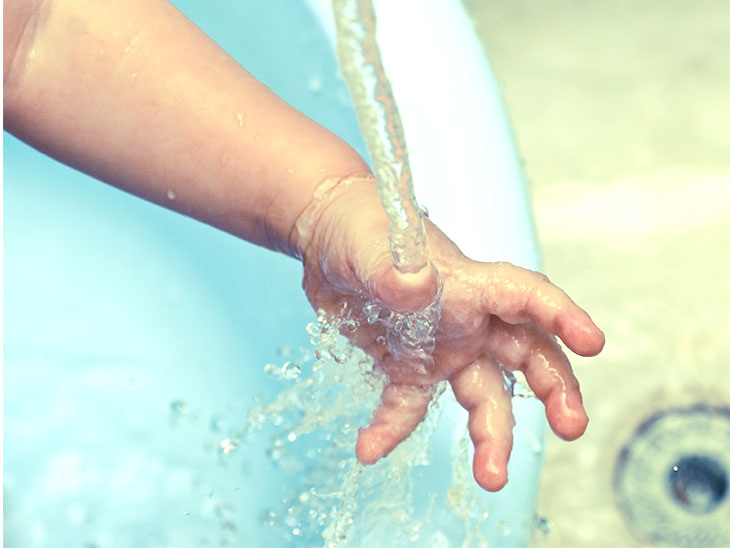 虫にさされた手を水で流している子供
