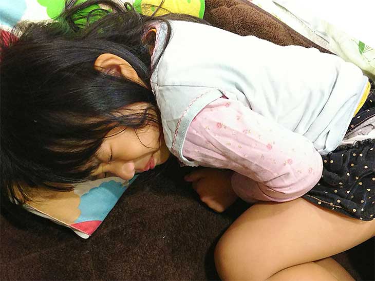 腹痛で横になってお腹を抑えながら丸くなっている女の子