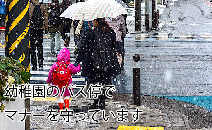 雪の中を幼稚園のバス停まで歩く親子