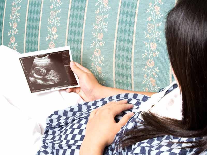 ソファで横になったままにエコー写真を見る妊婦さん