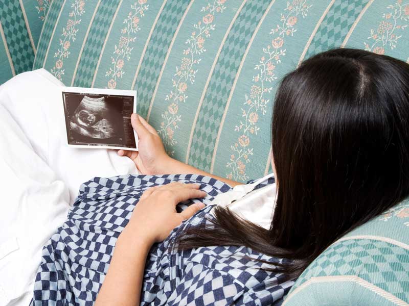 ソファでおなかにいる赤ちゃんの写真を見る妊婦さん