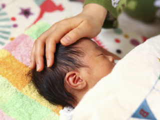 寝ている赤ちゃんと額に添えるママの手
